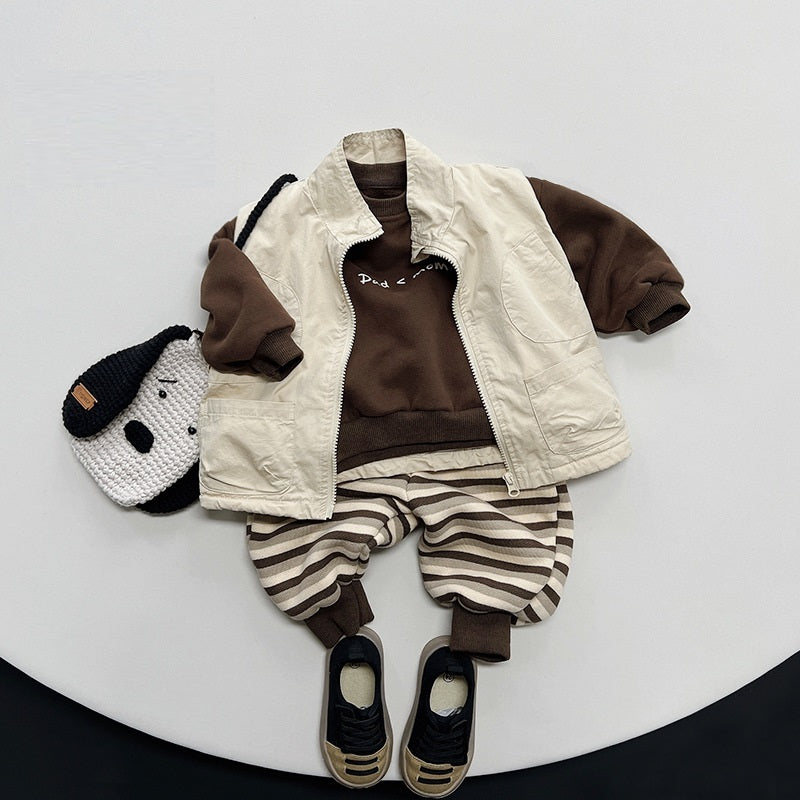 Brown slogan sweatshirt layered with cream vest and striped trousers