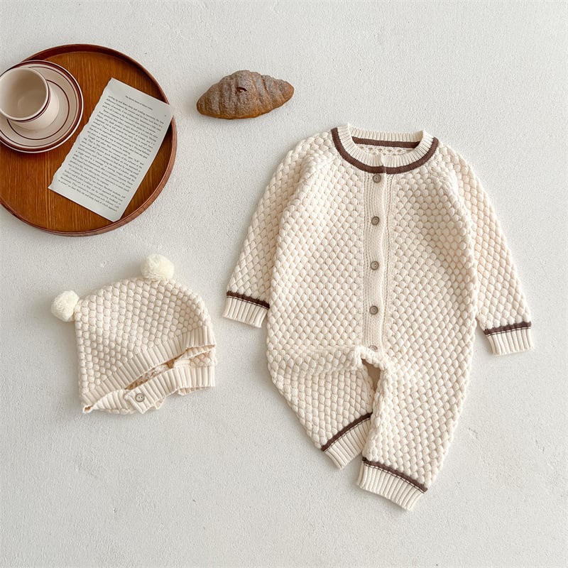 Cream popcorn knit baby romper with matching pom-pom bear hat, flat lay