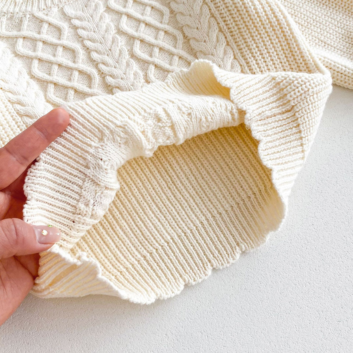 Close-up of soft cream cable knit texture and ribbed hem