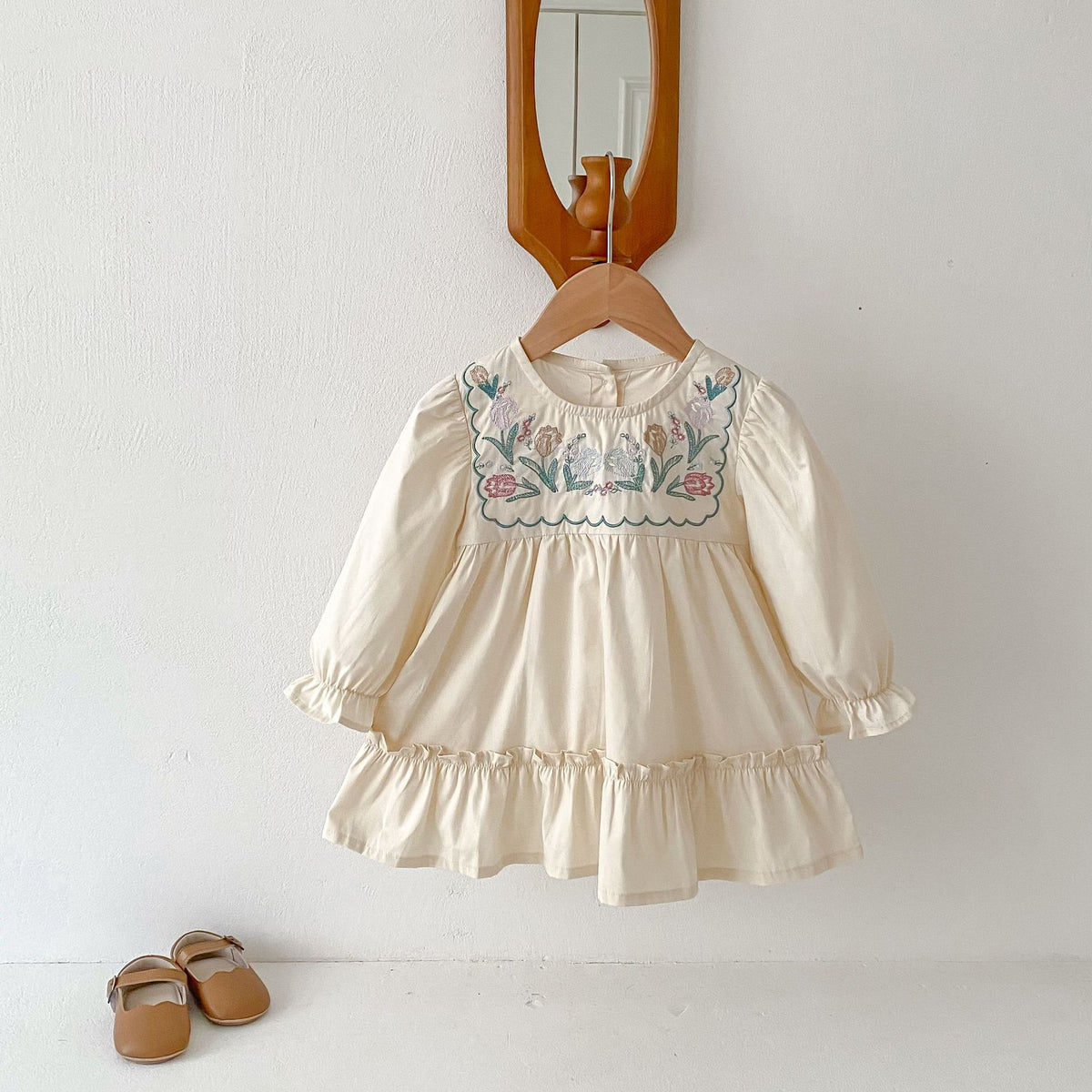 Cream long sleeve girls dress with floral embroidered yoke on a hanger