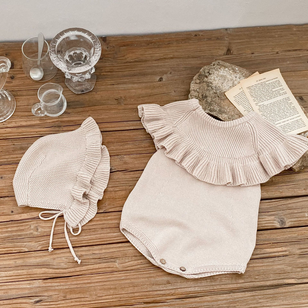 Cream knit romper and bonnet set laid on wooden table