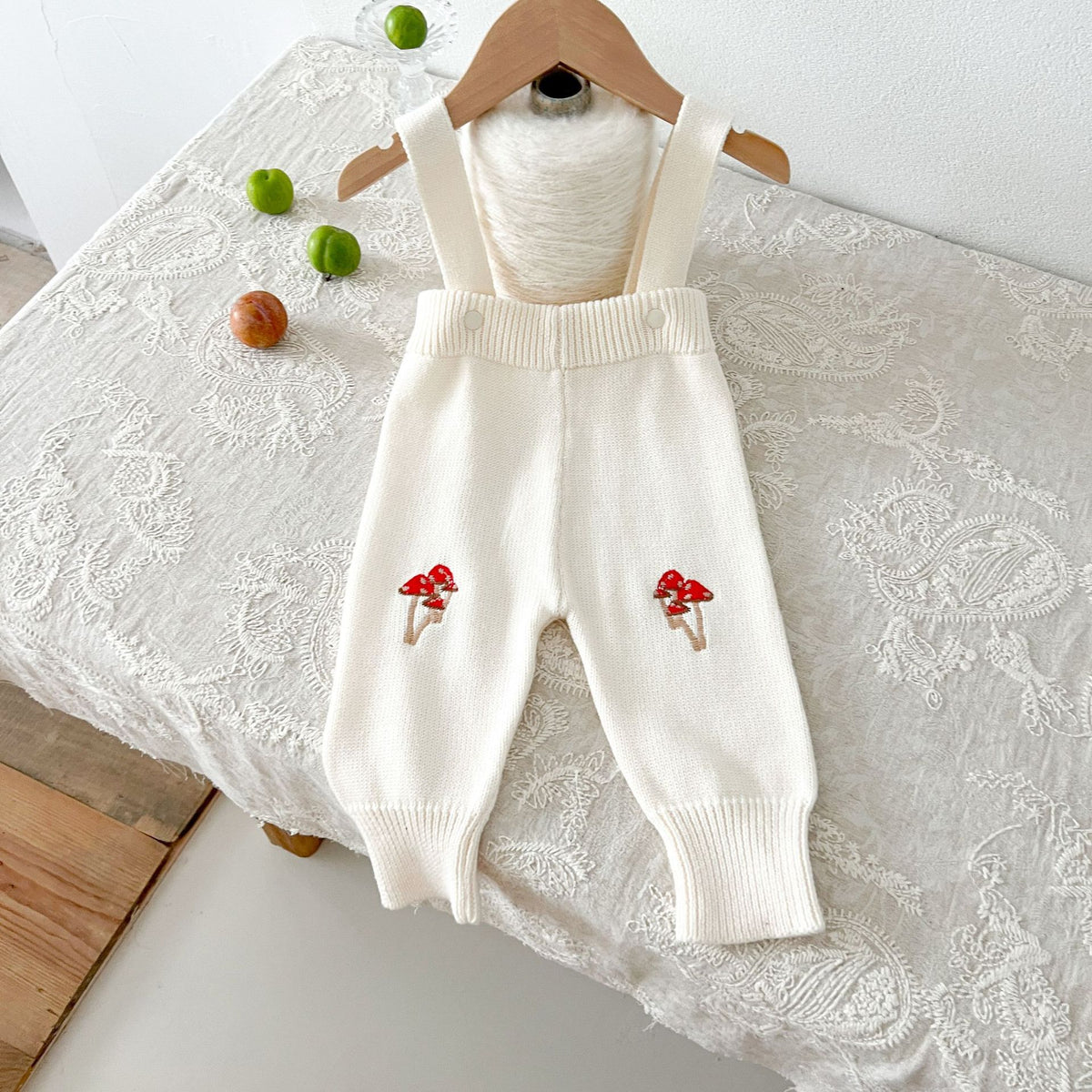Cream knit suspender pants with red mushroom embroidery on a hanger