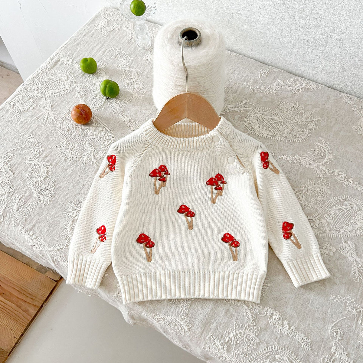Cream knit baby sweater with red mushroom embroidery on a hanger
