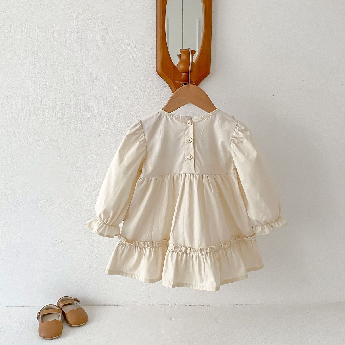 Back view of cream ruffle hem girls dress on a hanger
