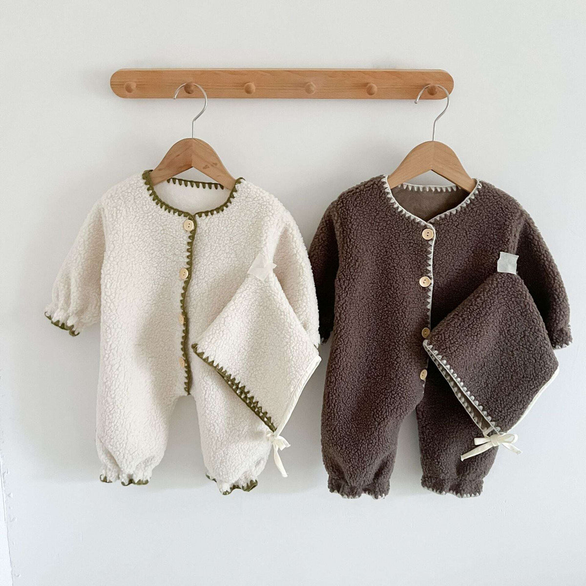 Ivory and cocoa fleece baby rompers hanging on wooden hangers