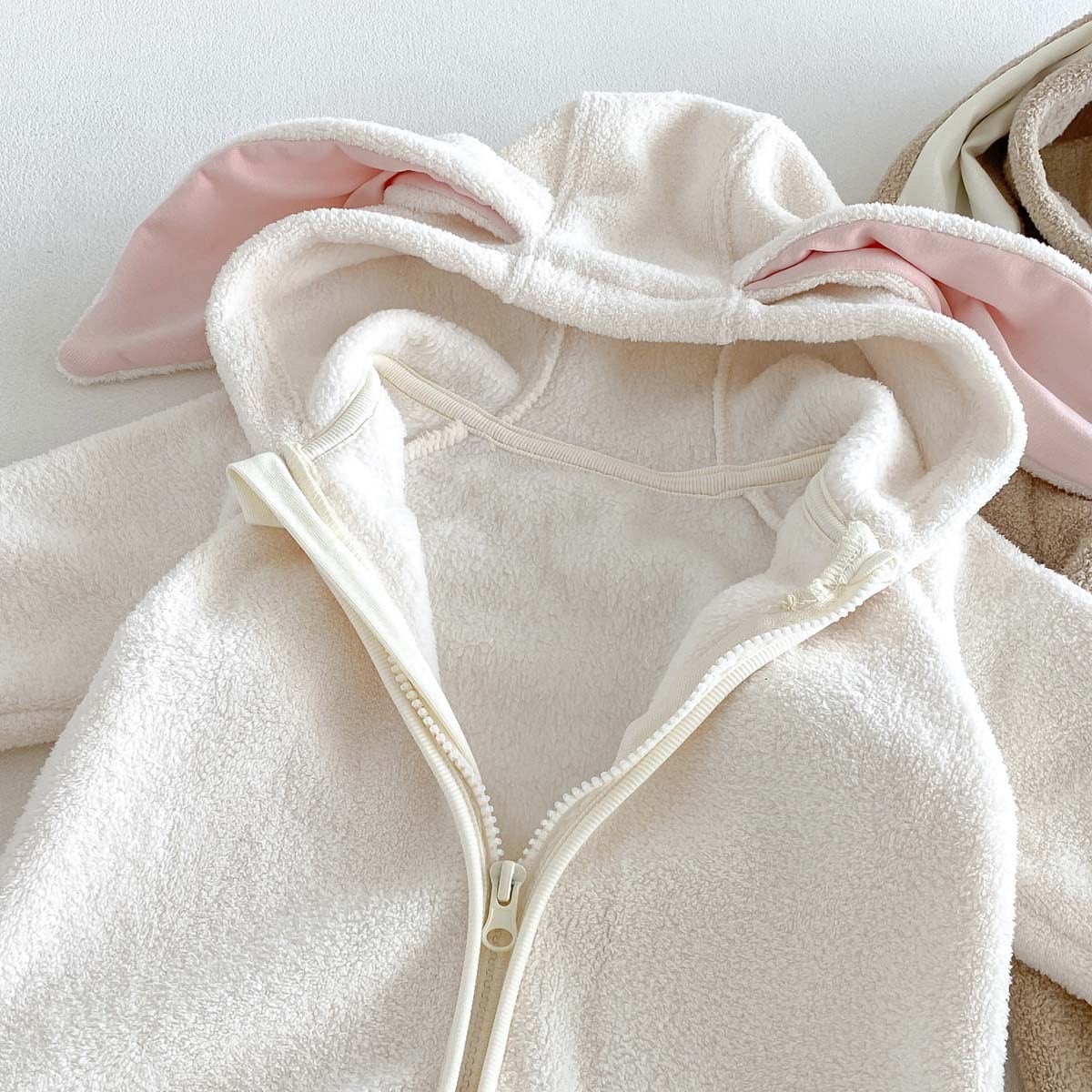 Close-up of the hood, pink-lined ears and zip on the ivory romper