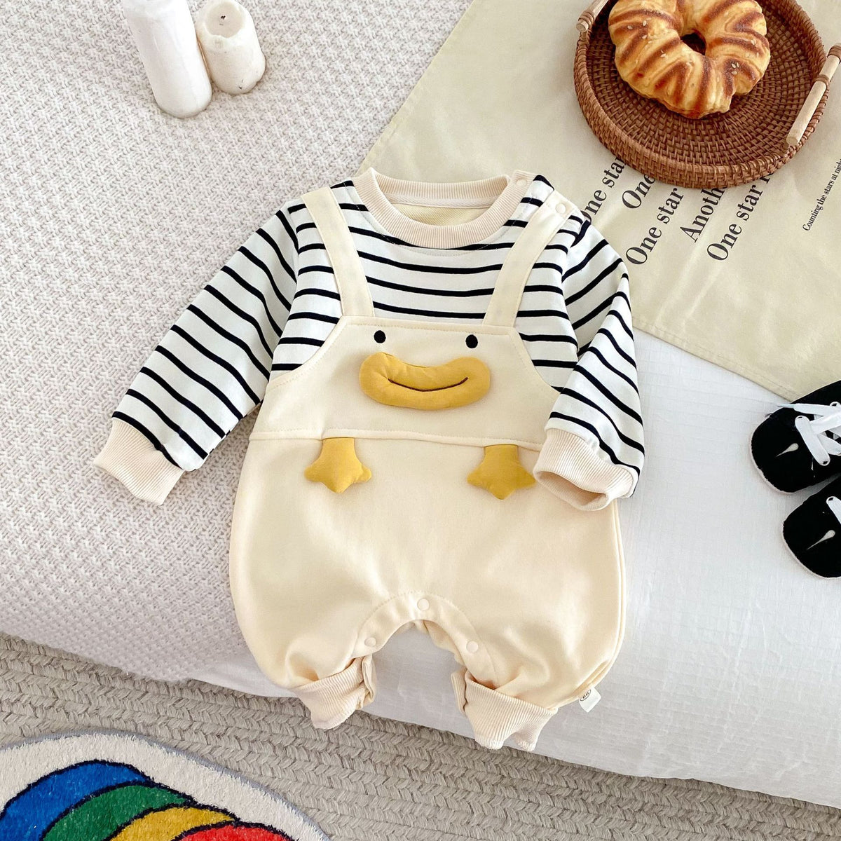 Striped baby jumpsuit with duck overall bib laid flat