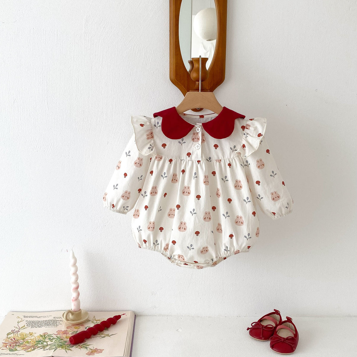 Cream floral baby romper with red petal collar on a hanger