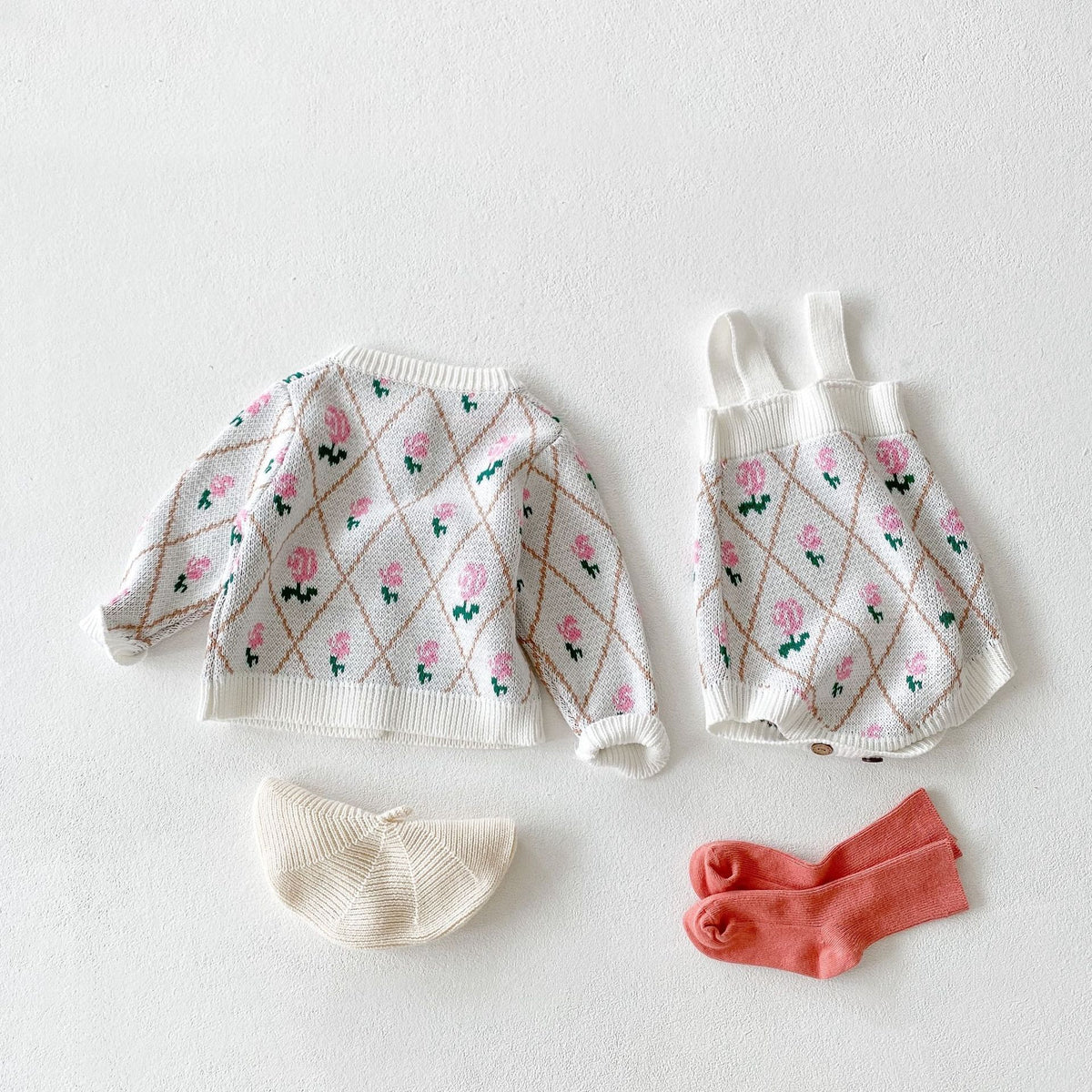Floral diamond knit cardigan and suspender romper laid flat with beret and socks