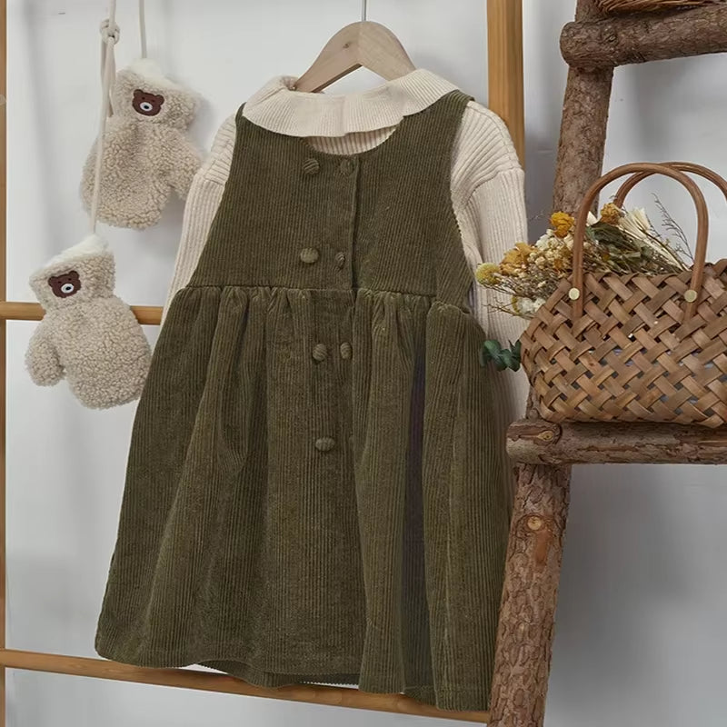 Olive green corduroy pinafore dress over cream blouse on a hanger