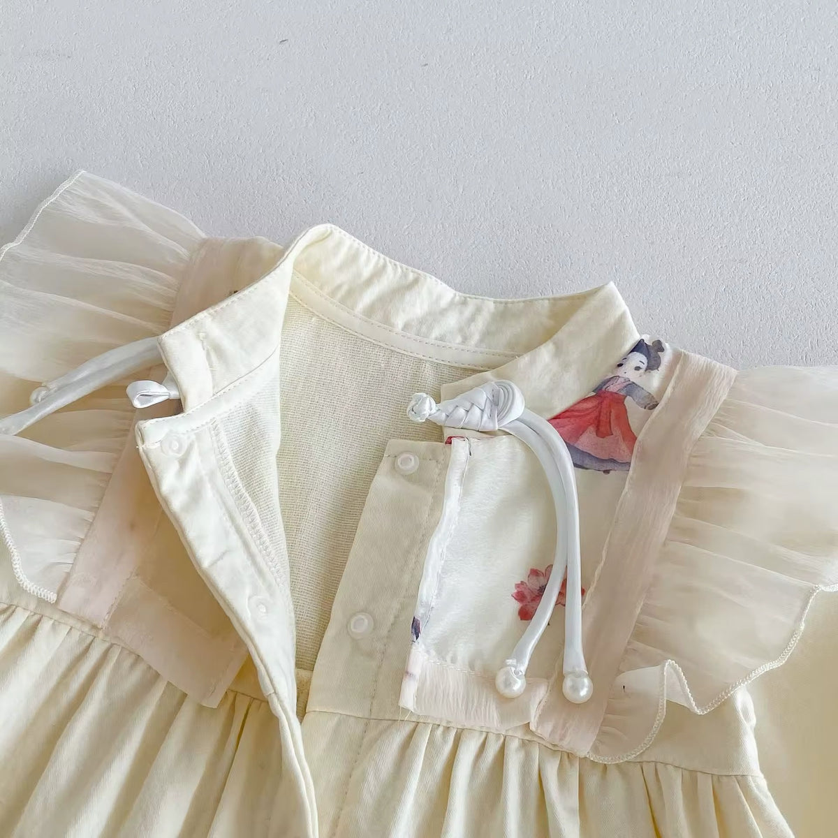 Close-up of button placket and tie on cream baby jumpsuit