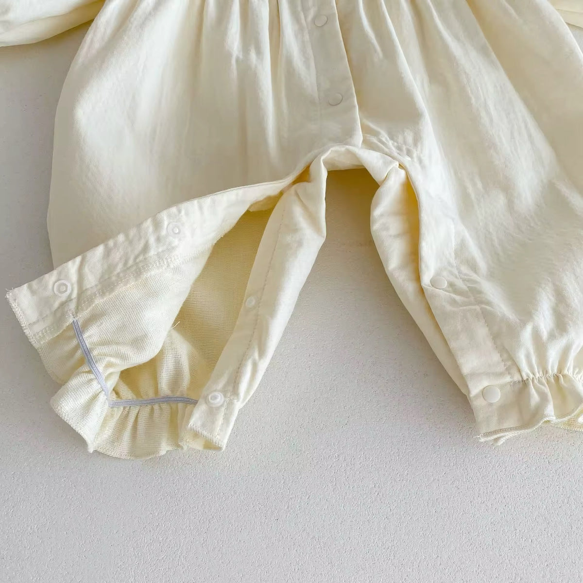 Snap closure along the legs of cream baby jumpsuit