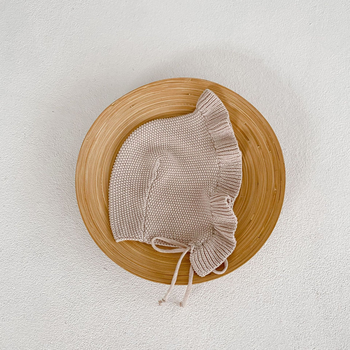 Ruffle knit baby bonnet on a wooden tray