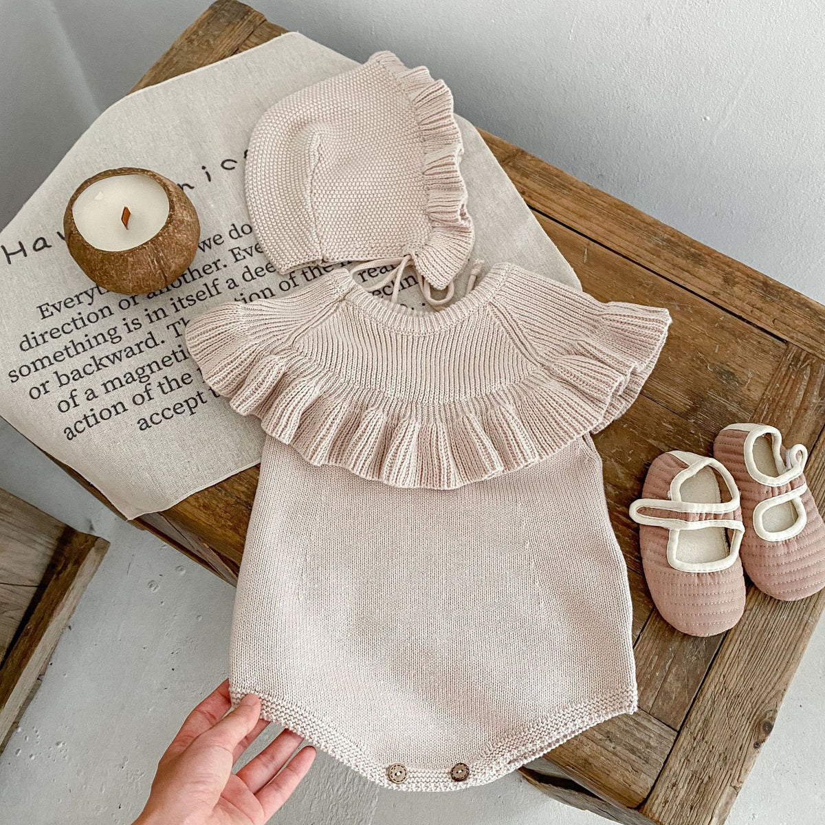 Oatmeal knit ruffle romper laid flat with baby shoes