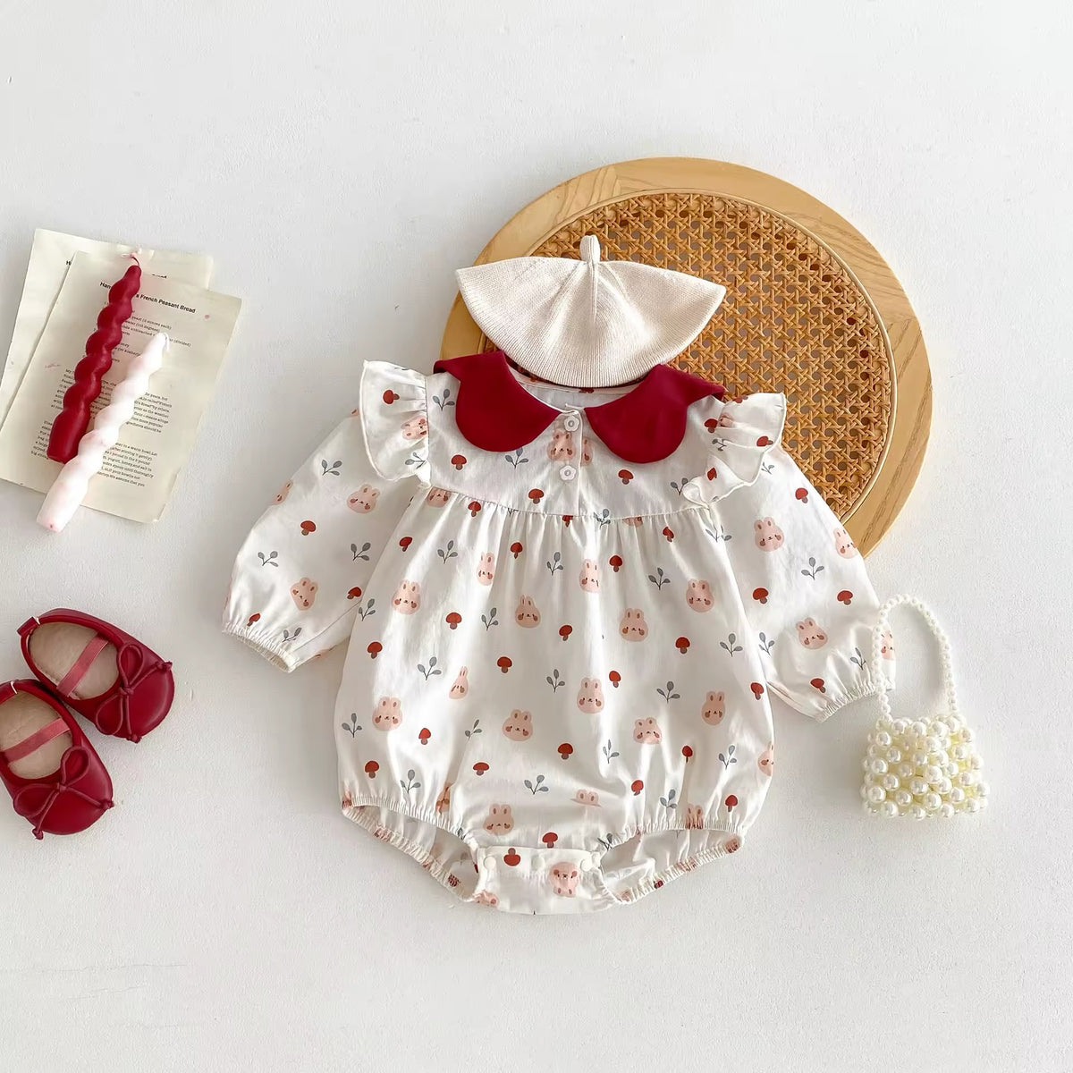Floral baby romper with red collar and matching bonnet, flat lay