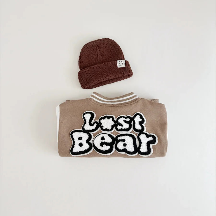 Folded varsity jacket showing Lost Bear print with beanie