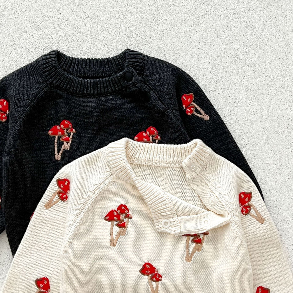 Close-up of red mushroom embroidery on black and cream knit sweaters
