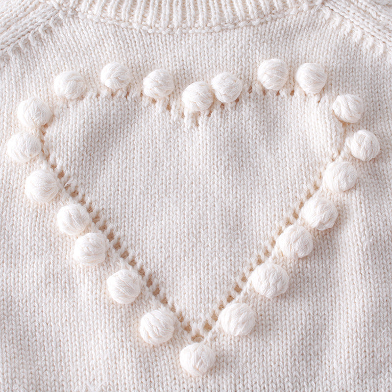 Close-up of pom-pom heart on cream knit