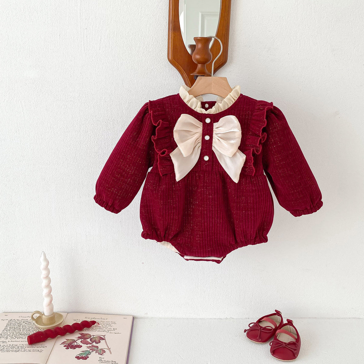 Red textured baby romper with cream bow on a hanger