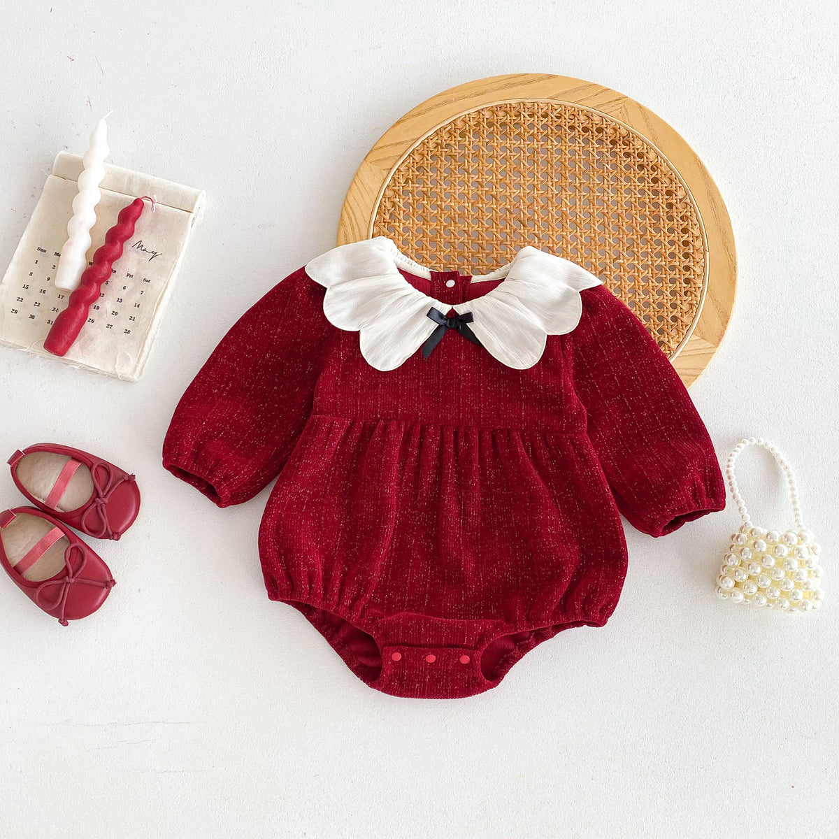 Red baby romper with white petal collar and black bow, flat lay