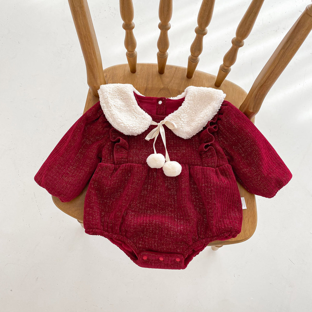 Red plush baby romper with pom-pom collar on a wooden chair