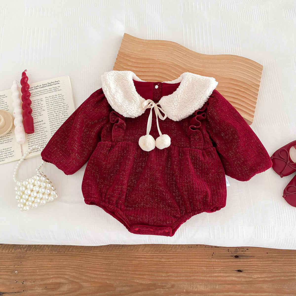 Red pom-pom collar baby romper on a wooden table