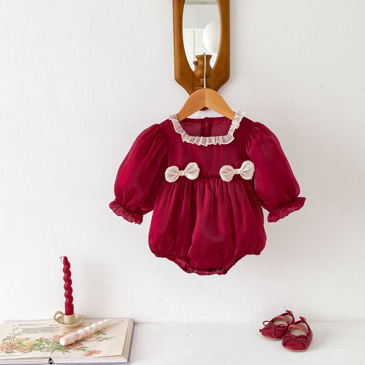 Ruby red baby romper with lace collar and cream bows on a hanger