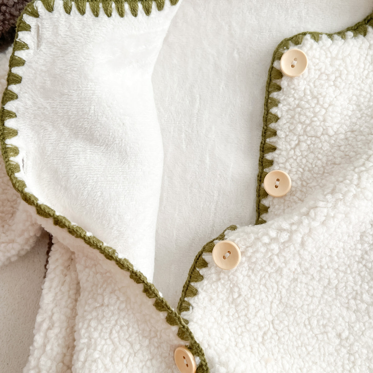 Close-up of buttons and stitched trim on white sherpa romper