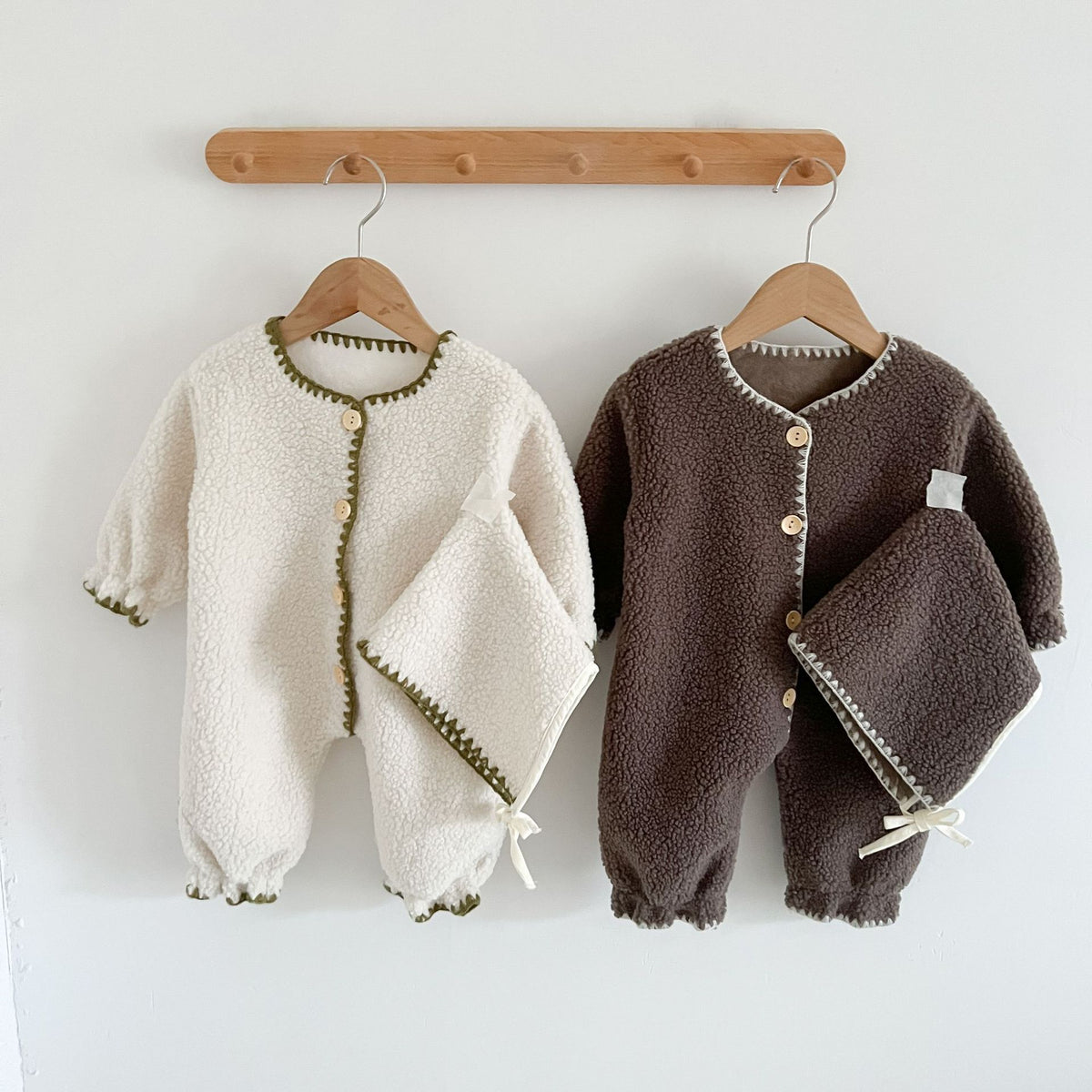White and brown teddy fleece rompers with bonnets on a peg rail