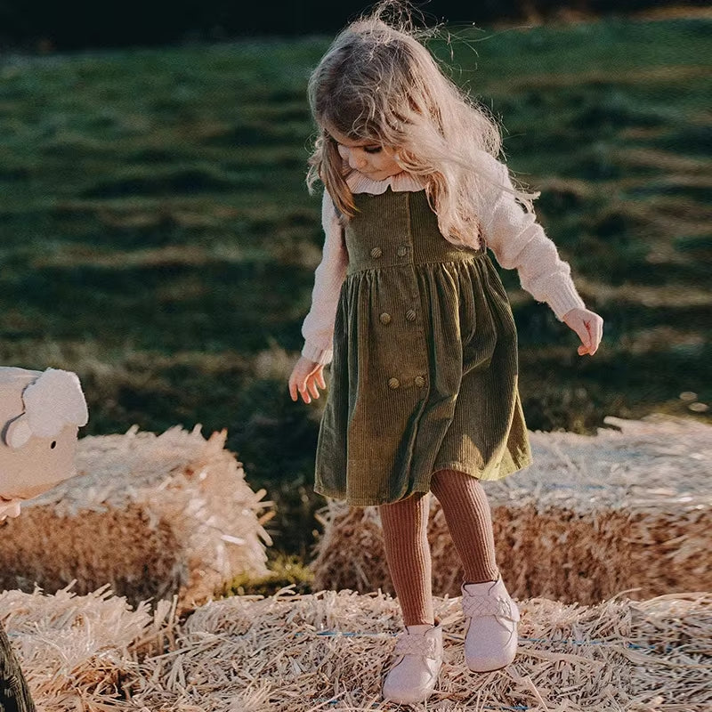 Toddler girl wearing green corduroy pinafore dress outdoors
