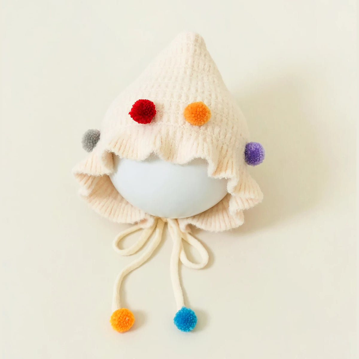 Cream pixie knit bonnet with confetti pom-poms and tie strings