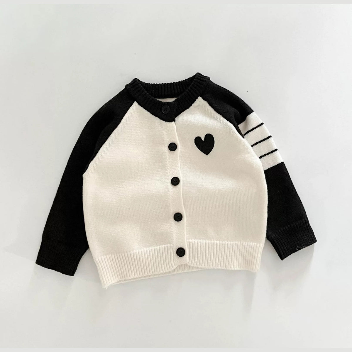 Cream knit baby cardigan with black raglan sleeves, sleeve stripes and a little heart