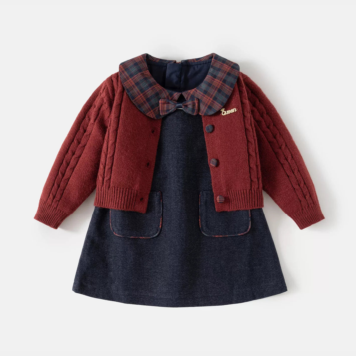 Girls cable-knit burgundy cardigan layered over a navy pinafore dress with plaid Peter Pan collar and bow, flat lay