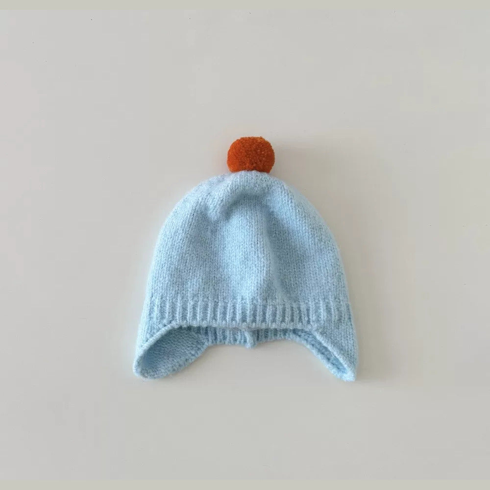 Sky blue knit baby earflap hat with orange pom-pom, flat lay