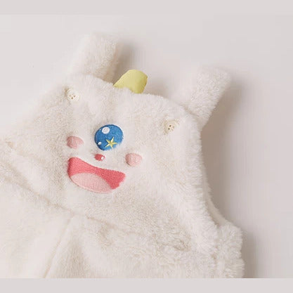 Close-up of the cream plush overalls bib with a playful monster face