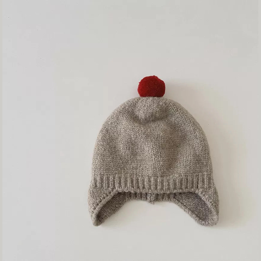 Taupe knit baby earflap hat with red pom-pom, flat lay