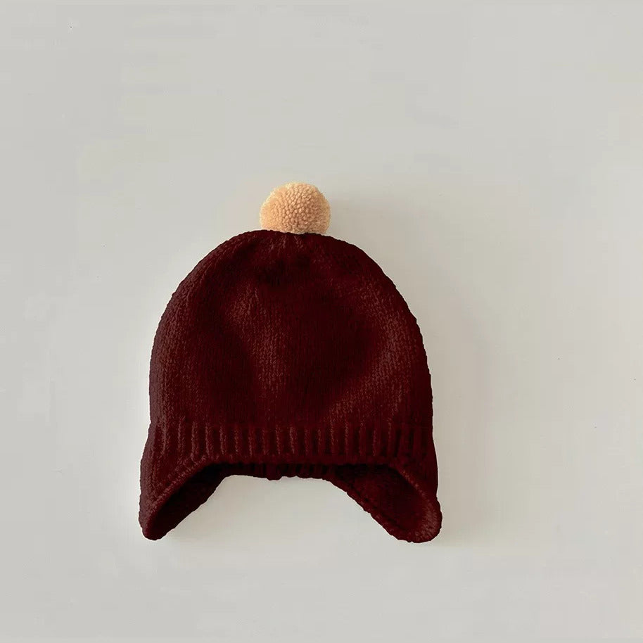 Cranberry red knit baby earflap hat with peach pom-pom, flat lay