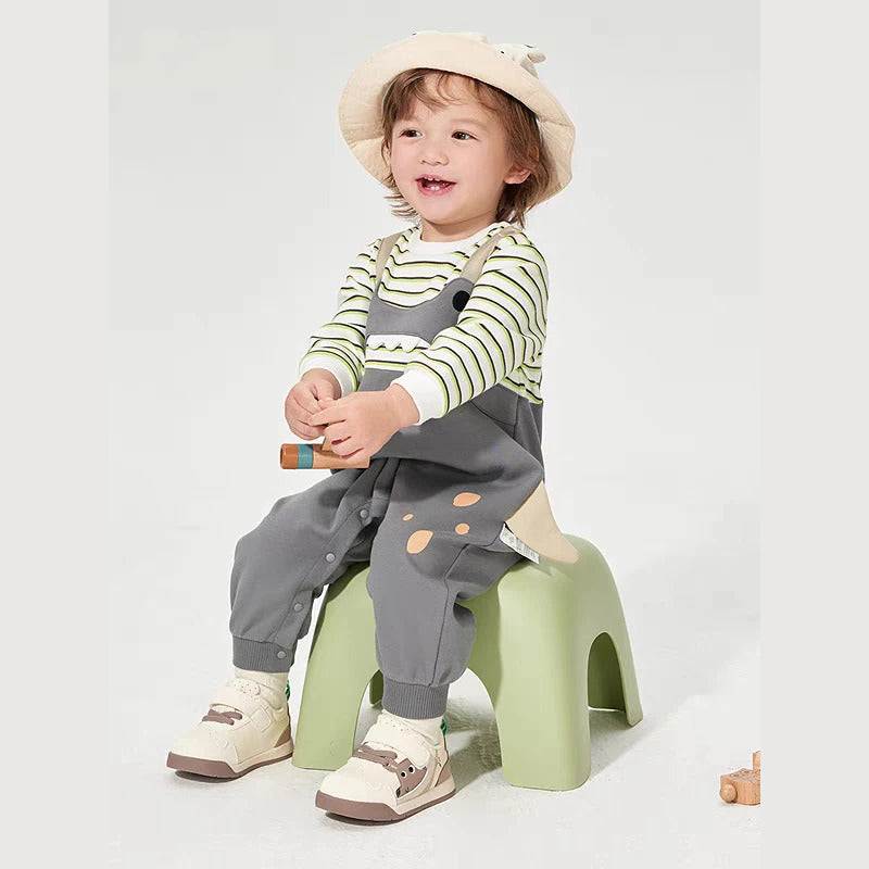 Smiling toddler in a grey dino stripe romper sitting on a green stool