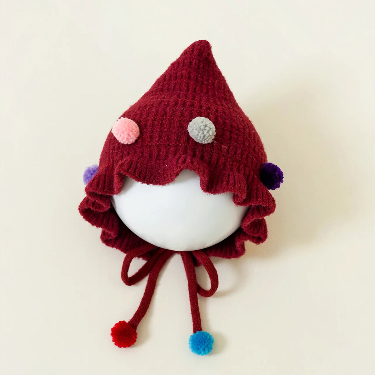Berry red pixie knit bonnet with confetti pom-poms and tie strings
