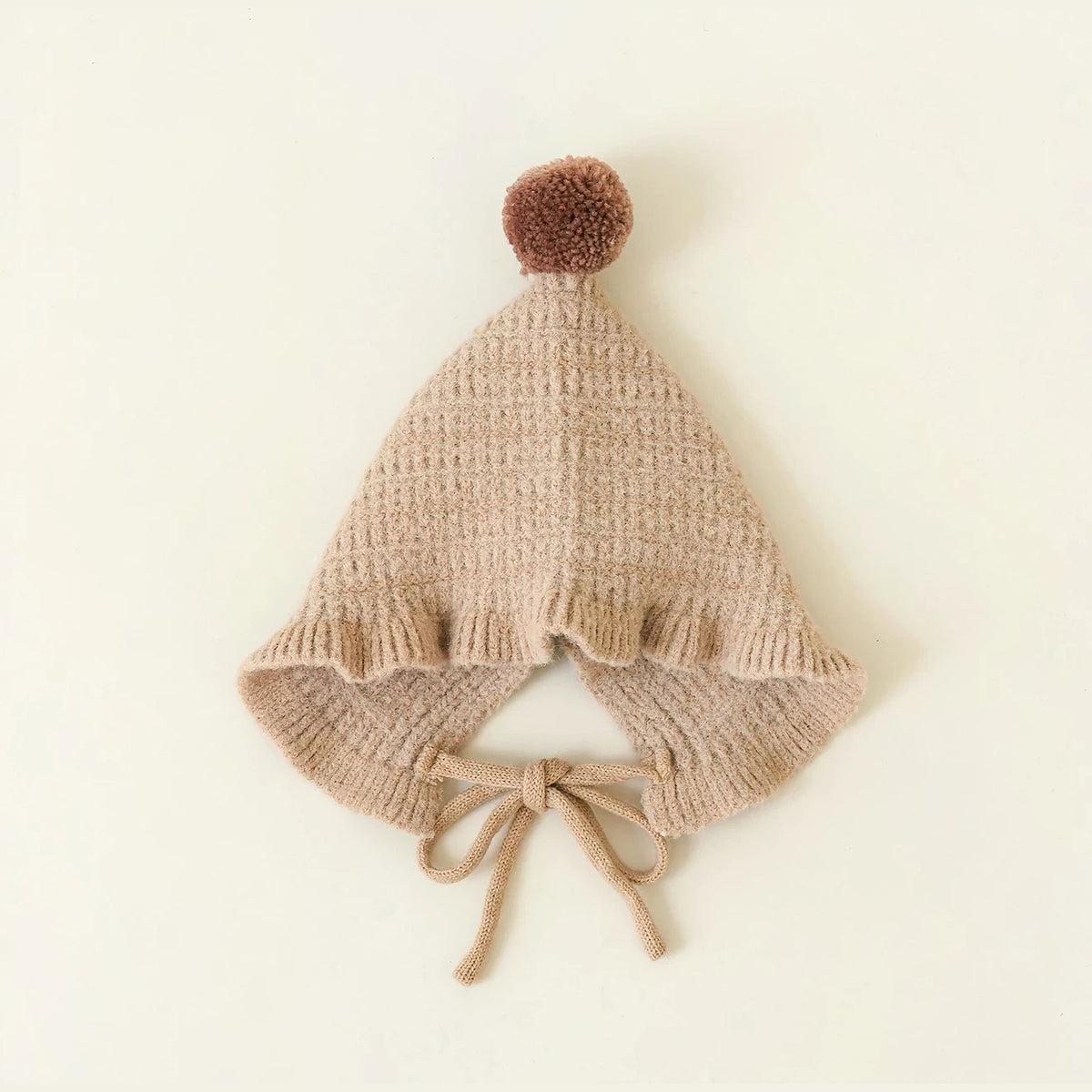 Latte pointed knit baby hat with a pom-pom on top, flat lay