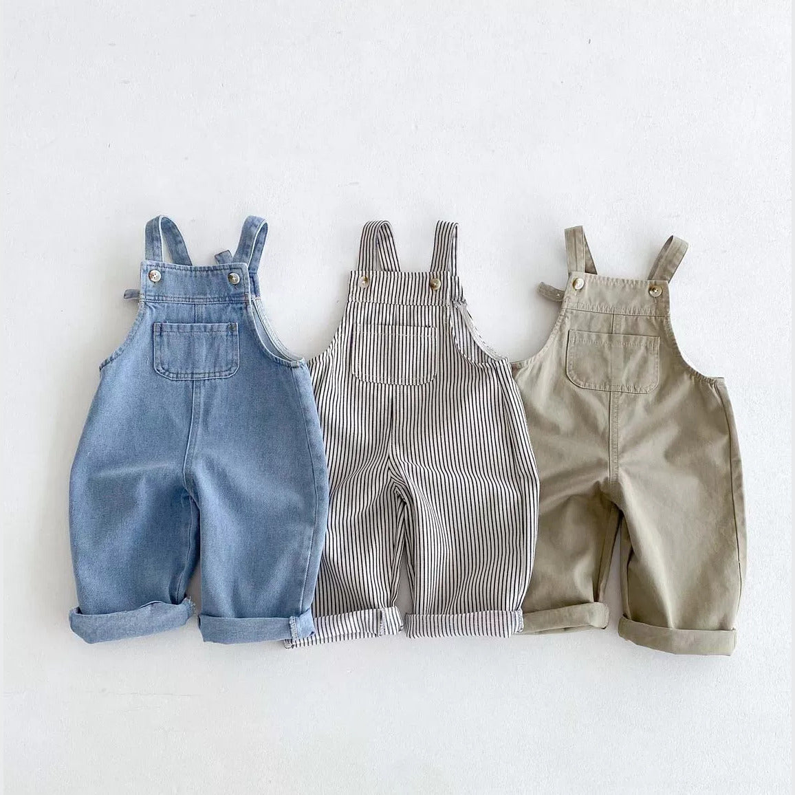 Denim, striped and khaki kids overalls laid side by side, flat lay