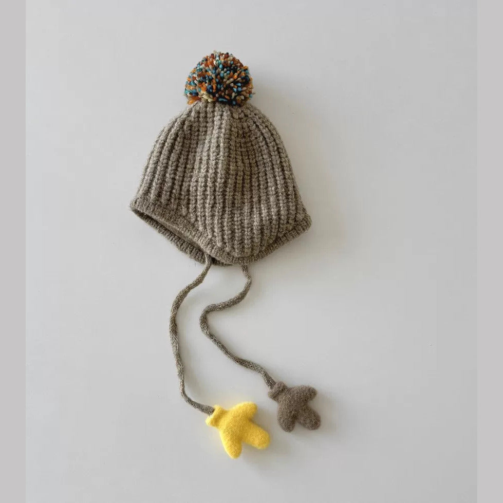 Khaki rib-knit toddler pom-pom hat with yellow and brown mitten charms on the ties