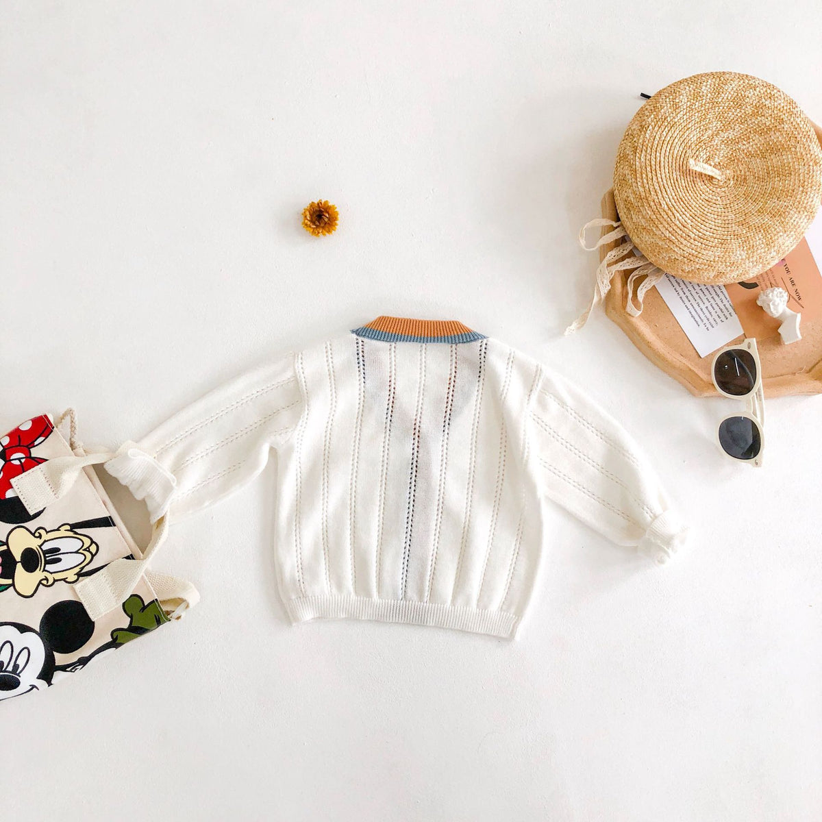 White knit cardigan laid flat with hat and toys