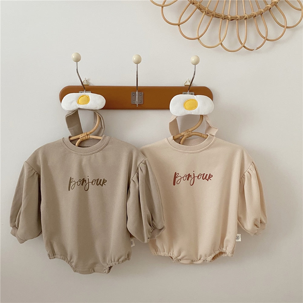 Brown and beige Bonjour bubble rompers on a wall hanger