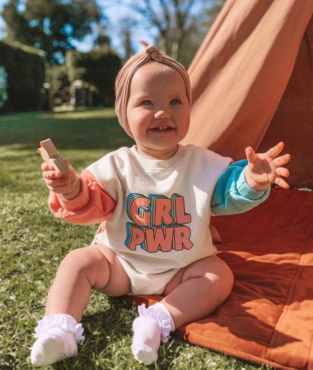 Baby in GRL PWR romper sitting outdoors