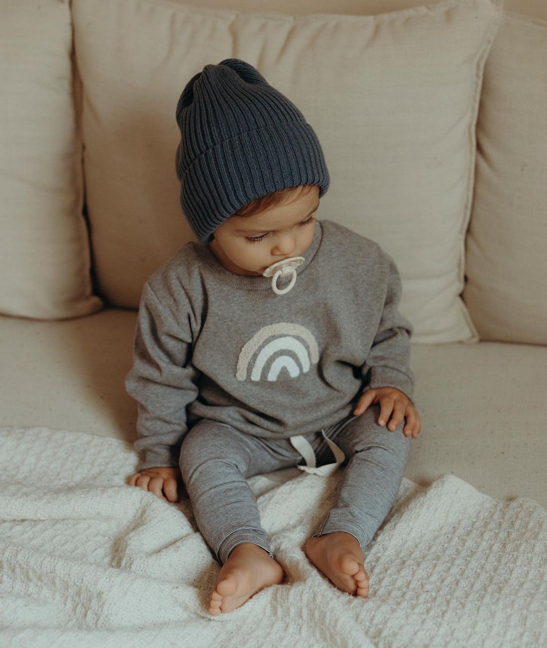 Baby in grey rainbow sweatshirt and joggers with beanie