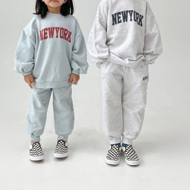 Two kids in light blue and gray NEW YORK tracksuits